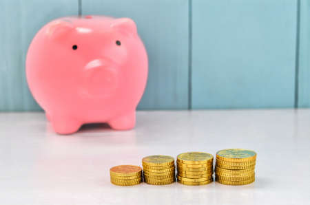 Stack of gold coins with pink piggy bank on white and blue wooden backgroundの写真素材