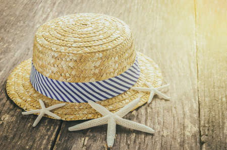 Beach concept - Straw Hat with white and blue striped on wooden table with starfishes and vintage sunlight toneの写真素材