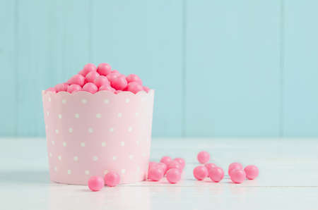 Pink candies in pink paper cup on white and blue wooden background - Pink bubblegum and candy
