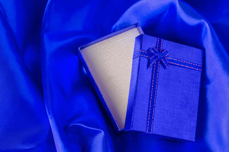 Opened blue gift box with blue ribbon bow on blue satin textile backgroundの写真素材