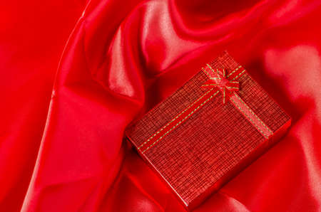 Red gift box with red ribbon bow on red satin textile backgroundの写真素材