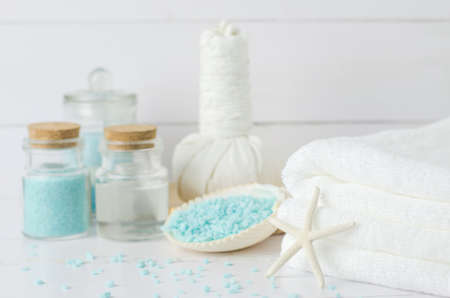 White towel with aromatherapy spa tools, coconut oil, blue aroma spa salt, herbal compress balls, seashells, starfish on white wooden backgroundの写真素材