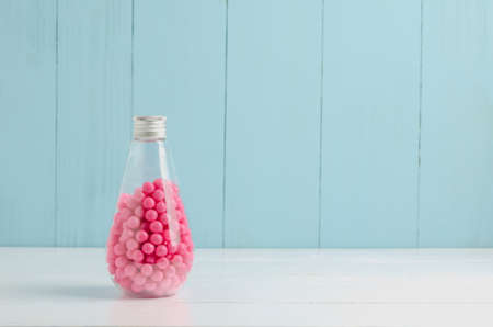Pink candies in transparent glass bottle on white and blue wooden background - Pink bubblegum and candyの写真素材