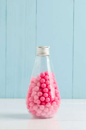 Pink candies in transparent glass bottle on white and blue wooden background - Pink bubblegum and...