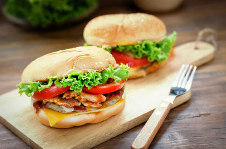 Close up of homemade cheese burger with grilled bacon and fresh vegetable, slice of tomato and lettuce on wooden boardの写真素材