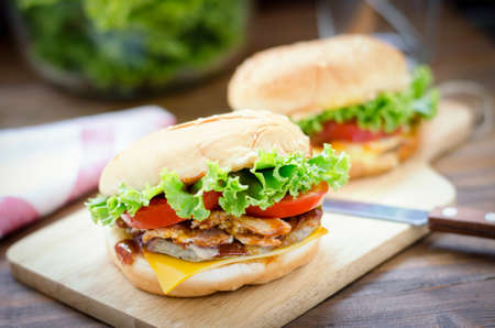Close up of homemade cheese burger with grilled bacon and fresh vegetable, slice of tomato and lettuce on wooden boardの写真素材