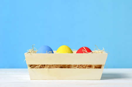Colorful easter eggs at wooden box on white and blue background, Easter backgroundの写真素材