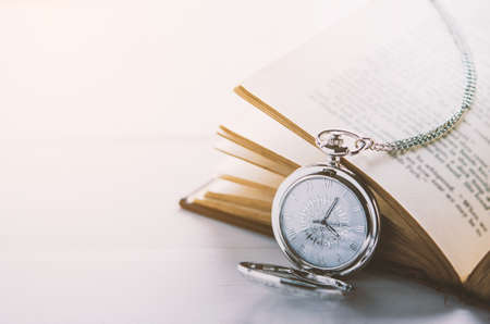 Close up of antique silver pocket watch and opened book on white table background with vintage lightの写真素材