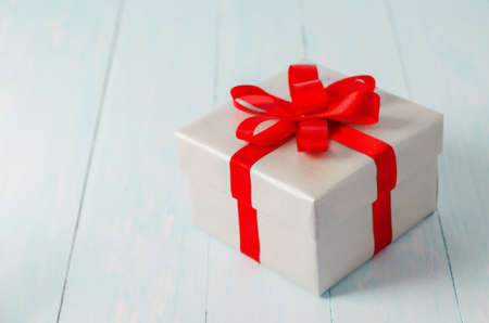 Close up of silver gift box with red ribbon bow on blue wooden backgroundの写真素材
