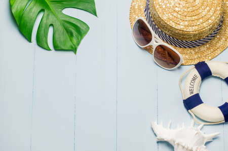 Straw hat with white sunglasses, lifebuoy and white seashell on blue wooden background with green leaves, Summer backgroundの写真素材