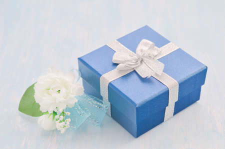 Close up of blue gift box with silver ribbon bow and Jasmine flower bouquet with blue ribbon bow on white and blue wooden background - Jasmine is the symbol of Mother's Day in Thailand.の写真素材