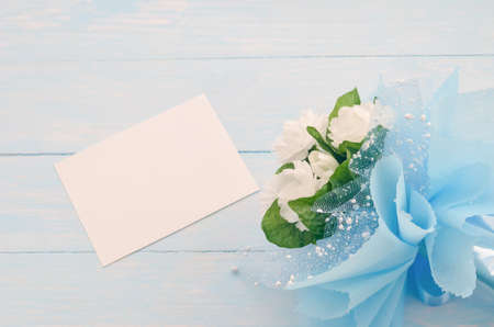 Blank white greeting card paper and beautiful Jasmine flower bouquet with blue ribbon bow on white...