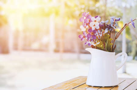 Artificial purple and white flowers at white vase on wooden table with vintage and sunlight tone