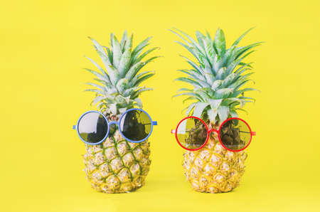 Pineapples with red and blue sunglasses on yellow background - Summer backgroundの写真素材