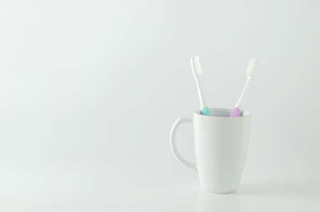 Green and purple toothbrush with white ceramic mug on white backgroundの写真素材