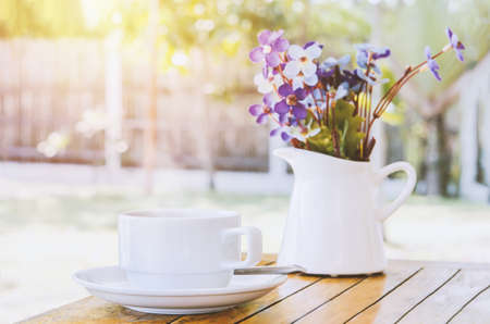 Close up of white coffee cup and flowers vase on wooden table with vintage and sunlight toneの写真素材