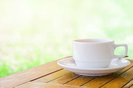 Cup of coffee on wooden table with green light bokeh backgroundの写真素材