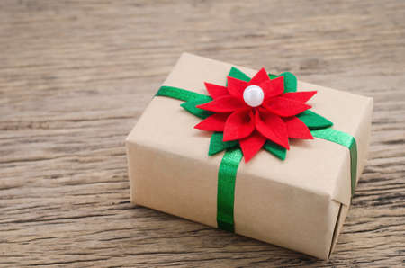 Brown gift box with red and green Christmas Poinesettia flower ribbon bow on wooden tableの写真素材