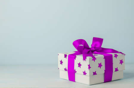 White gift box with purple star pattern and purple ribbon bow on blue wooden background - Christmas backgroundの写真素材