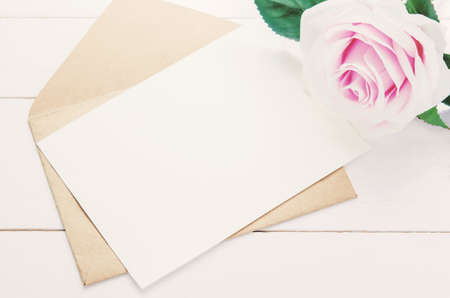 Blank white greeting card with brown envelope and purple rose flower on white wooden backgroundの写真素材