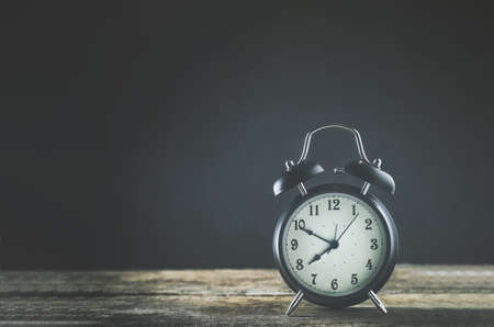 Close up of black Alarm clock on wooden table with vintage and vignette toneの写真素材