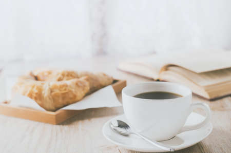Close up of white coffee cup with croissant on wooden table with vintage and vignette toneの写真素材