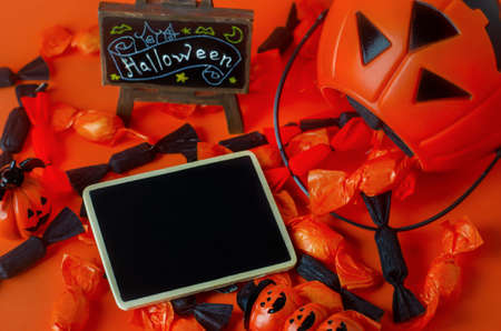 Halloween background - Blank black wooden tag with pumpkin bag, black and orange candies on orange backgroundの写真素材