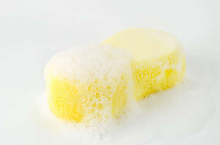 Close up of yellow sponge with soapsuds and bubbles on white backgroundの写真素材