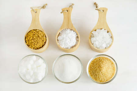 Different kinds of sugar in glass and wooden bowl on white wooden table - brown, white, crystal, cube and Icing sugarの写真素材