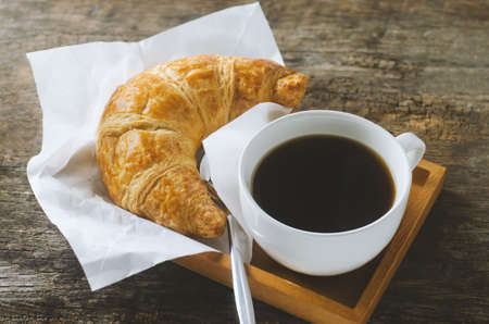 Close up of black coffee with croissant on wooden table with vintage and vignette toneの写真素材