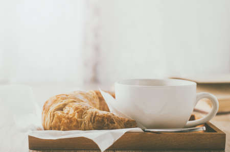 Close up of white coffee cup with croissant on wooden table with vintage and vignette toneの写真素材