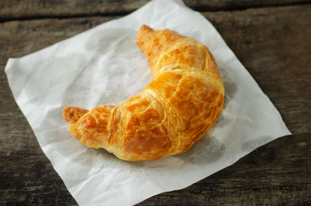 Close up of croissant with white paper on wooden tableの写真素材