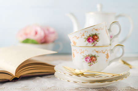 Close up of cup of tea with book, teapot and rose flowers on blue background with vintage tone - Afternoon tea party conceptの写真素材