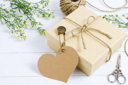 Brown gift box with heart tag label on wooden table with white daisy flower and vintage pinの写真素材
