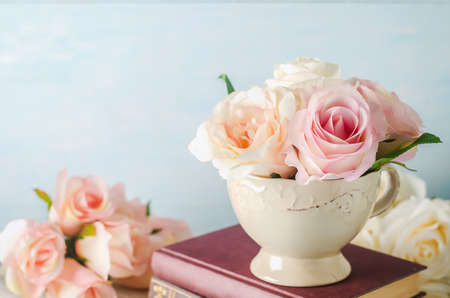 Artificial pink rose flowers in vintage cup with books on blue background with vintage toneの写真素材