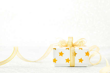 Close up of white gif box with golden star pattern and gold ribbon bow on bokeh background - Christmas backgroundの写真素材