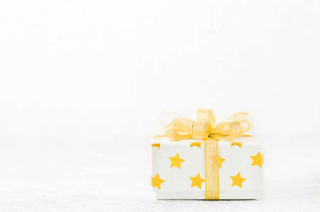 Close up of white gif box with golden star pattern and gold ribbon bow on bokeh background -...