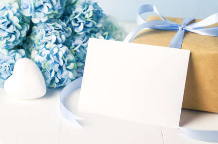 Close up of empty white greeting card  with brown recycle gift box and blue Hydrangea flowers on blue wooden background with soft vintage toneの写真素材