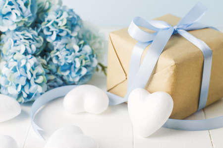 Close up of brown recycle gift box with white heart and blue Hydrangea flowers on blue wooden background with soft vintage toneの写真素材