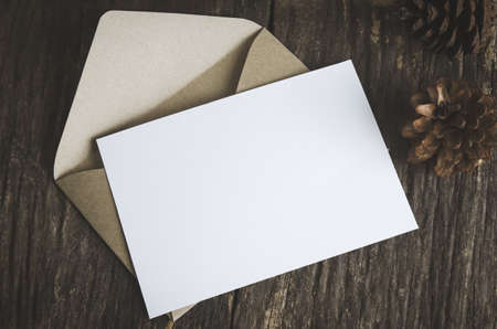 Blank white paper card with brown envelop and pine cones on old wooden table with vintage and vignette toneの写真素材