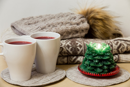 Two caps of mulled wine and a candle in front of a pile of winter clothesの写真素材