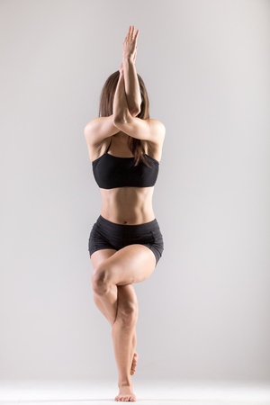 Beautiful sporty yogi girl practices yoga asana, Garudasana,Eagle Pose on grey background, low key shotの写真素材
