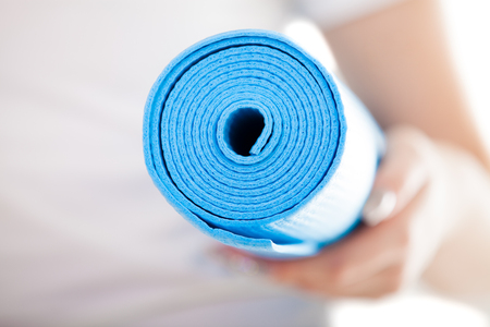 Close up, white woman hands holding folded blue yoga, pilates mat for fitness training. Healthy life, keep fit, weight loss concepts. Focus on mat, white t-shirt on backgroundの写真素材