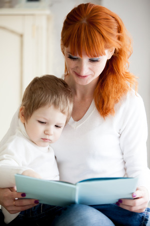 Red-haired young mom reading book to her little son. Focus on childの写真素材