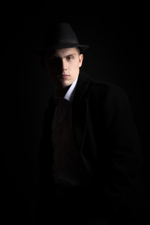 Good-looking guy in hat and coat with confident serious look, fashionable and handsome, low key studio shot against black backgroundの写真素材
