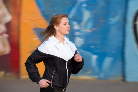Beautiful sporty runner girl in sportswear running at speed in the morning city beside bright...