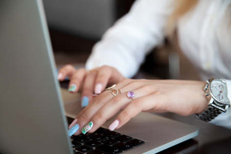 Modern office girl hands on laptop using touch pad and keyboard with rings on fingers and colorful manicure, close upの写真素材