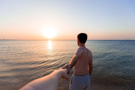 Young man leading by hand his lover, at the sea coast in sunlight, follow me conceptの写真素材