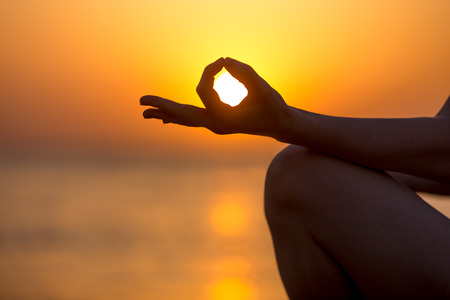 Young woman fingers in yogic Jnana mudra, close up, copy space. Relaxation, meditation on sea at sunset or sunriseの写真素材