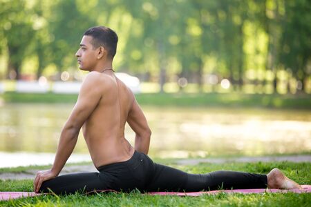 Profile of Handsome sporty Indian young man exercising on river bank in park, doing yoga, fitness or...